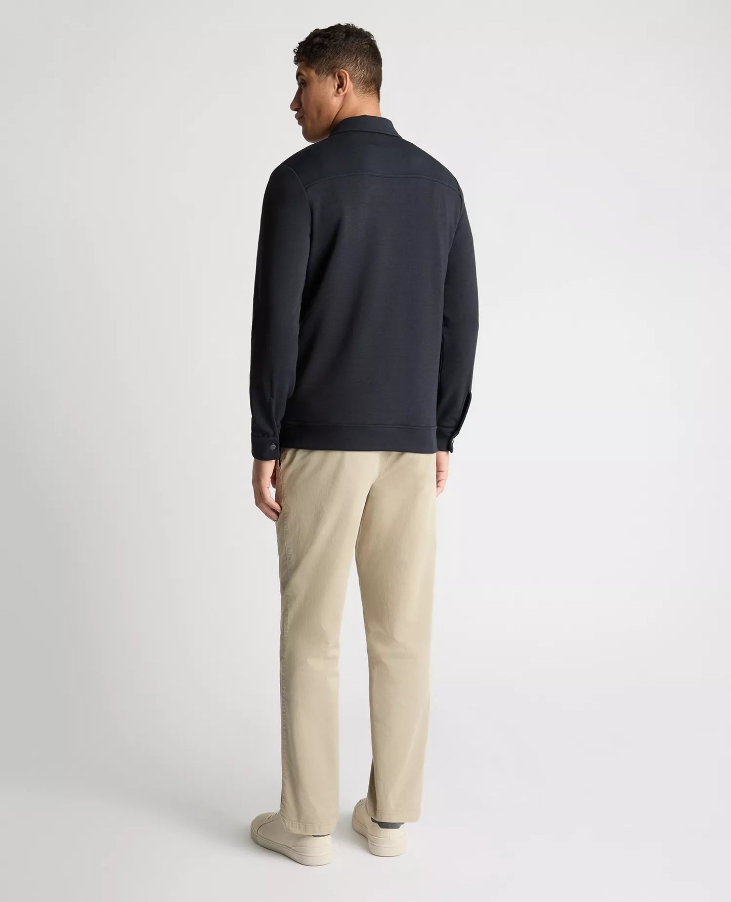 Man wearing a dark jacket and beige pants on a white background