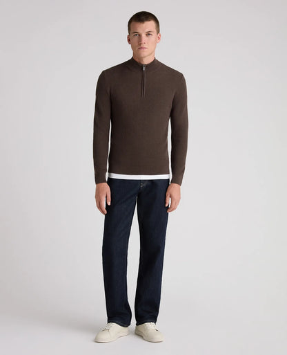 A man modeling a dark brown quarter-zip knit sweater with a white hem detail, paired with dark blue jeans and off-white sneakers, against a light gray studio background.