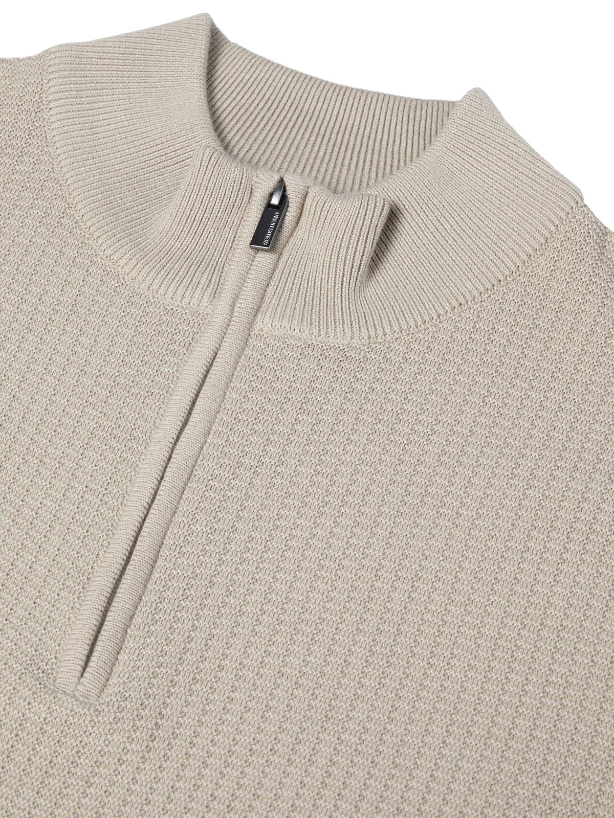Close-up of a beige ribbed knit quarter-zip sweater with a stand collar and a small black zipper pull.
