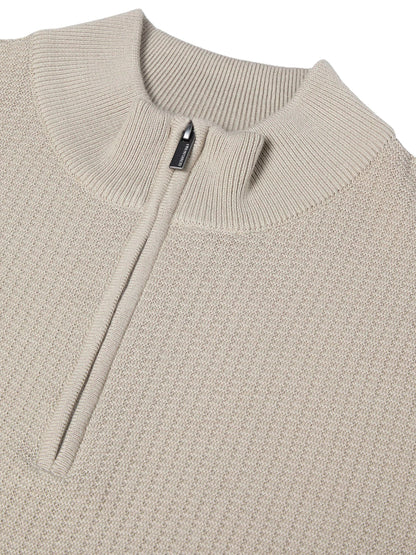 Close-up of a beige ribbed knit quarter-zip sweater with a stand collar and a small black zipper pull.