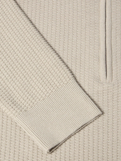 Close-up of a cream-colored knit sweater showing the waffle texture, a ribbed cuff, and part of a vertical ribbed placket.