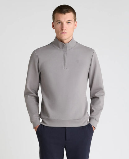 A man wearing a light gray quarter-zip pullover sweatshirt and navy blue trousers, standing against a light gray studio background.