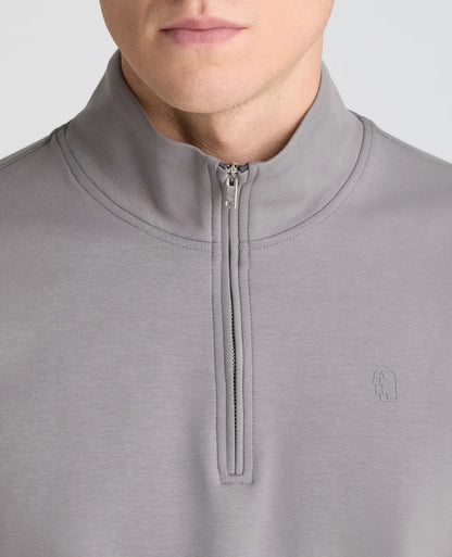 Close-up of a person wearing a light gray quarter-zip pullover with a mock neck collar and a small tonal embroidered logo on the left chest, against a plain light gray background.