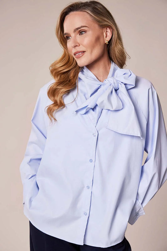 Woman wearing a light blue blouse with a bow detail on a beige background