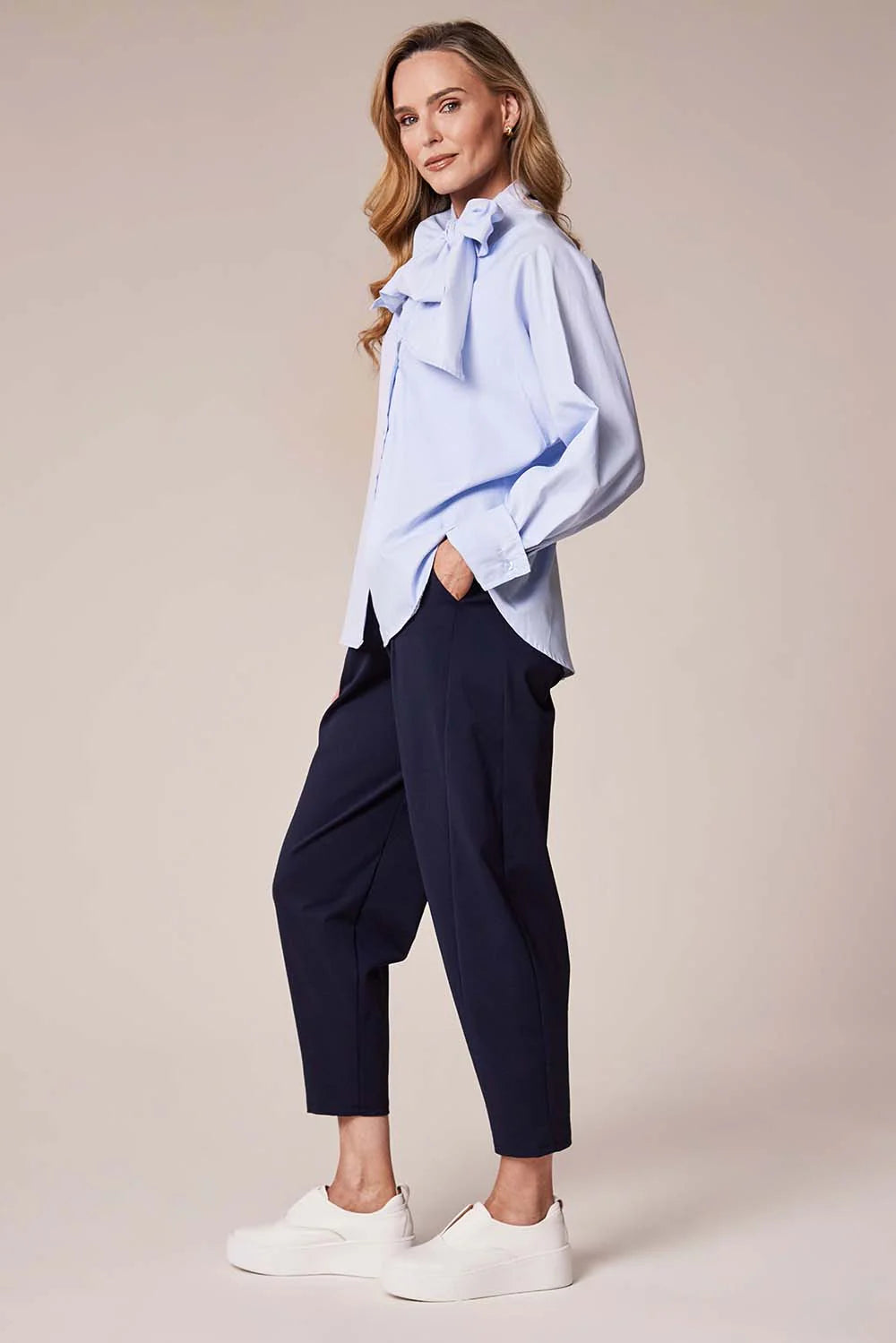 Woman wearing a light blue shirt and navy pants on a beige background