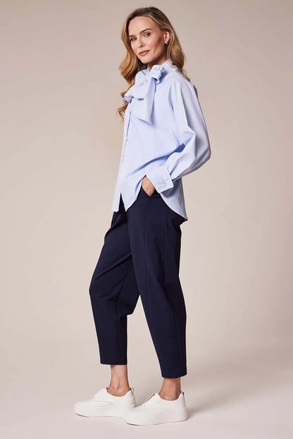 Woman wearing a light blue shirt and navy pants on a beige background