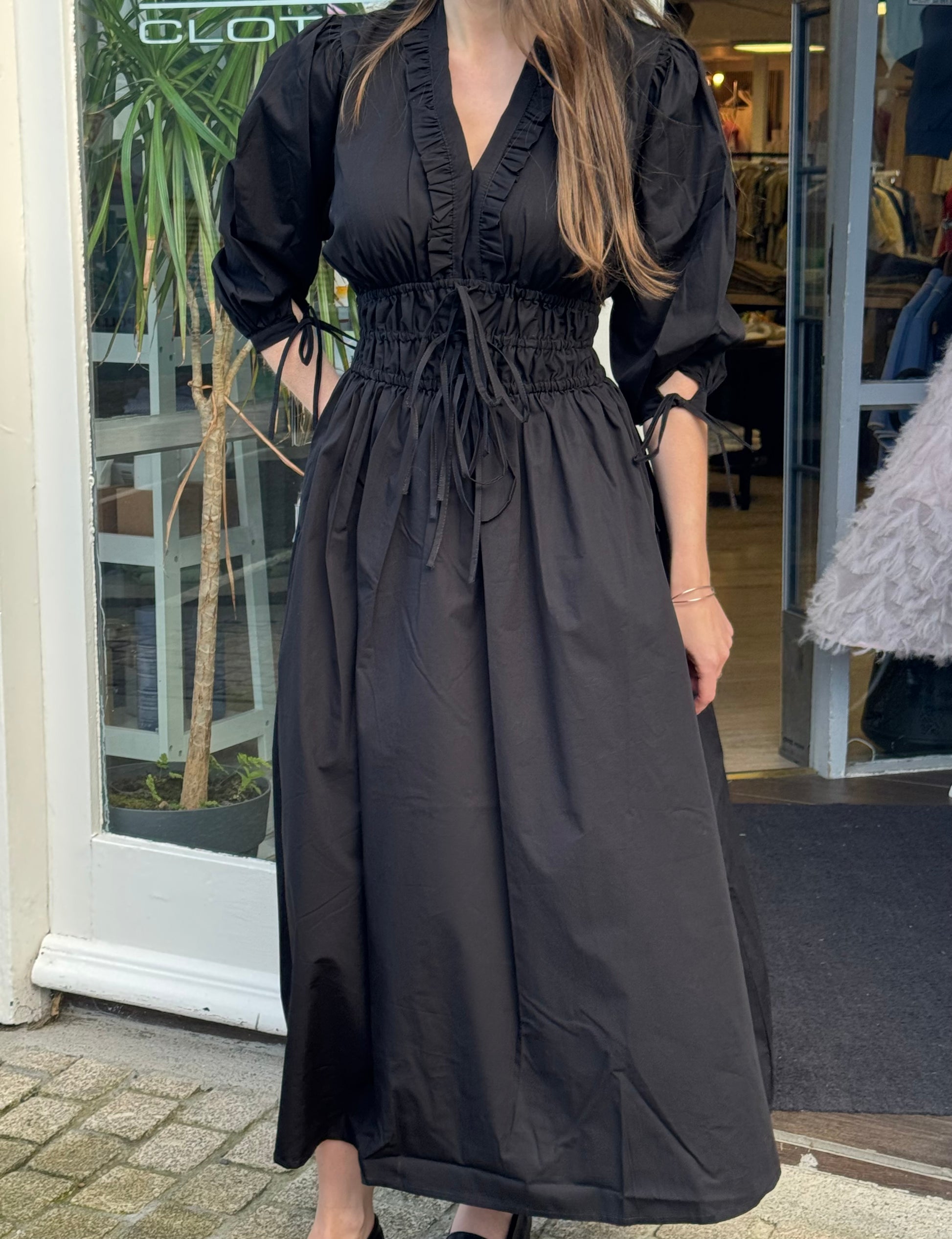 Woman wearing a black dress standing outside a store.