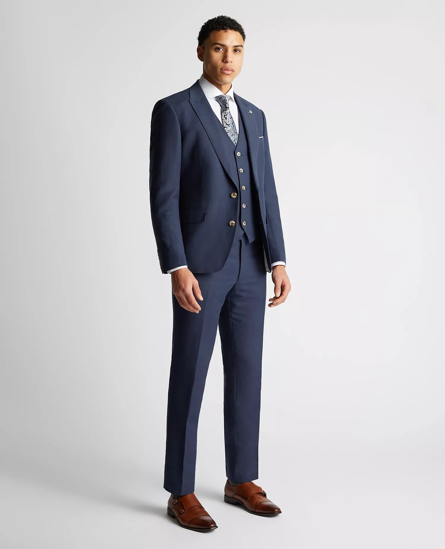 Man wearing a blue suit with brown shoes on a light gray background