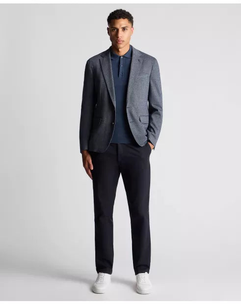 Man wearing a gray blazer, navy shirt, black pants, and white sneakers on a light gray background