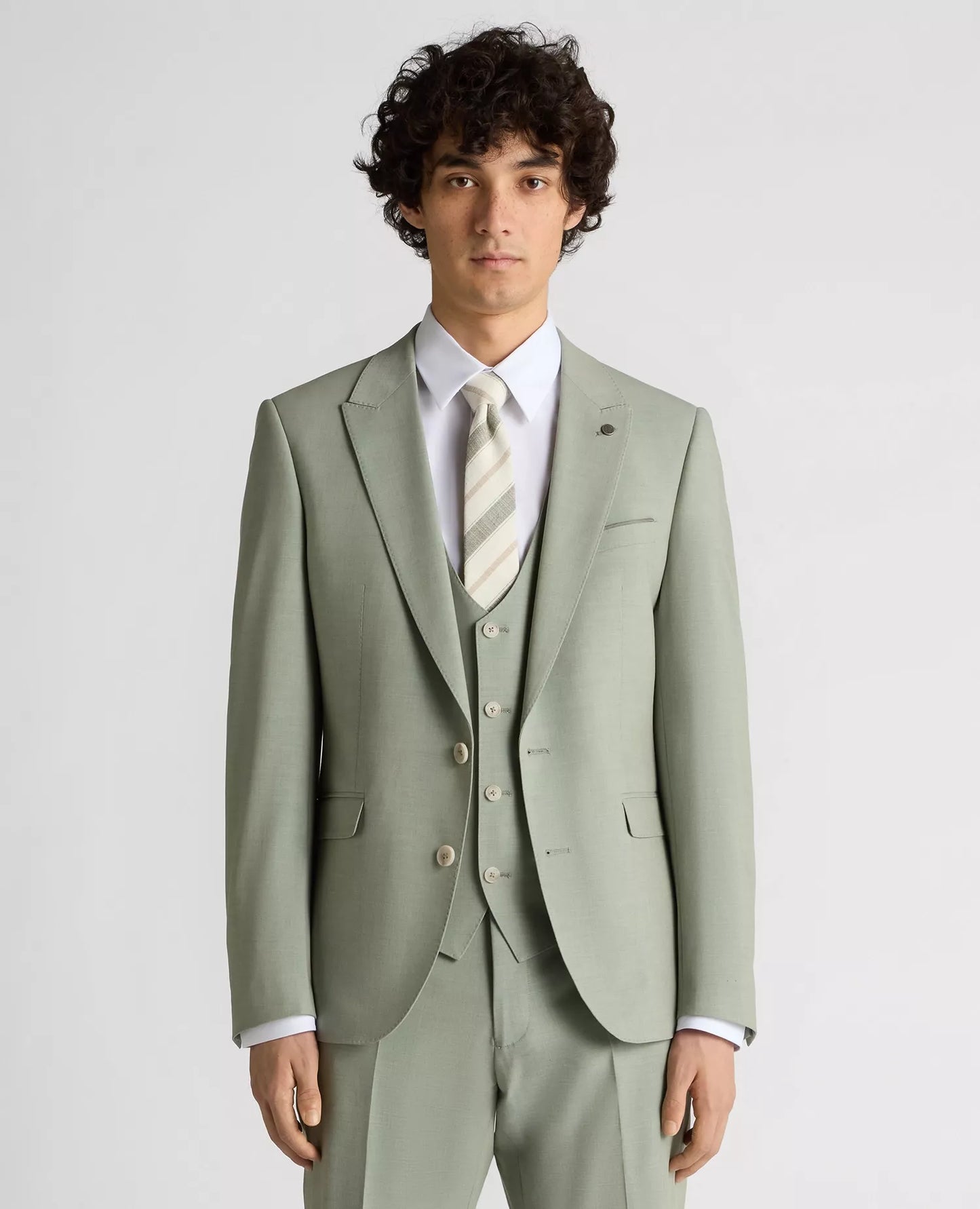 Man wearing a light green suit with a white shirt and patterned tie on a plain background