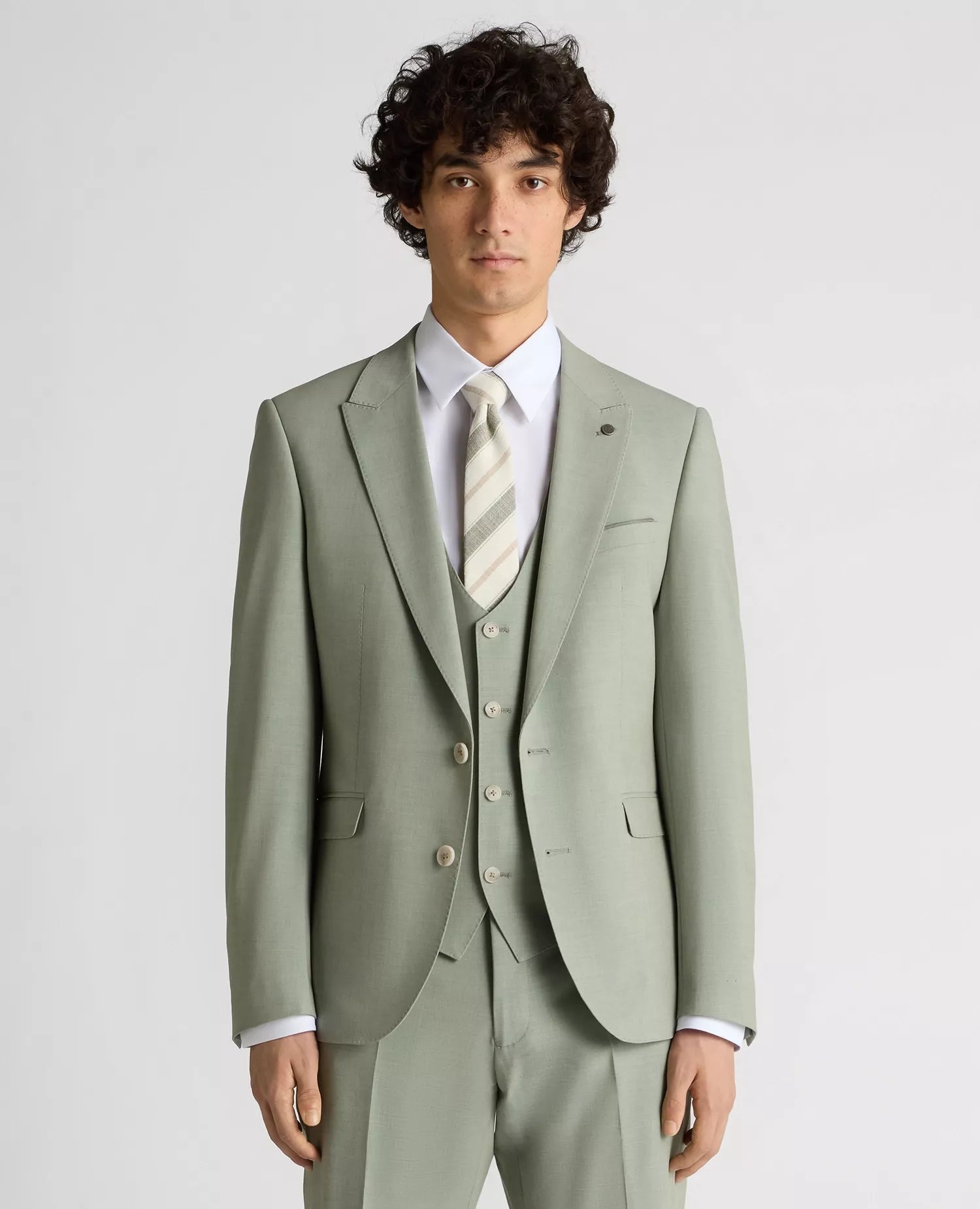 Man wearing a light green suit with a white shirt and patterned tie on a plain background