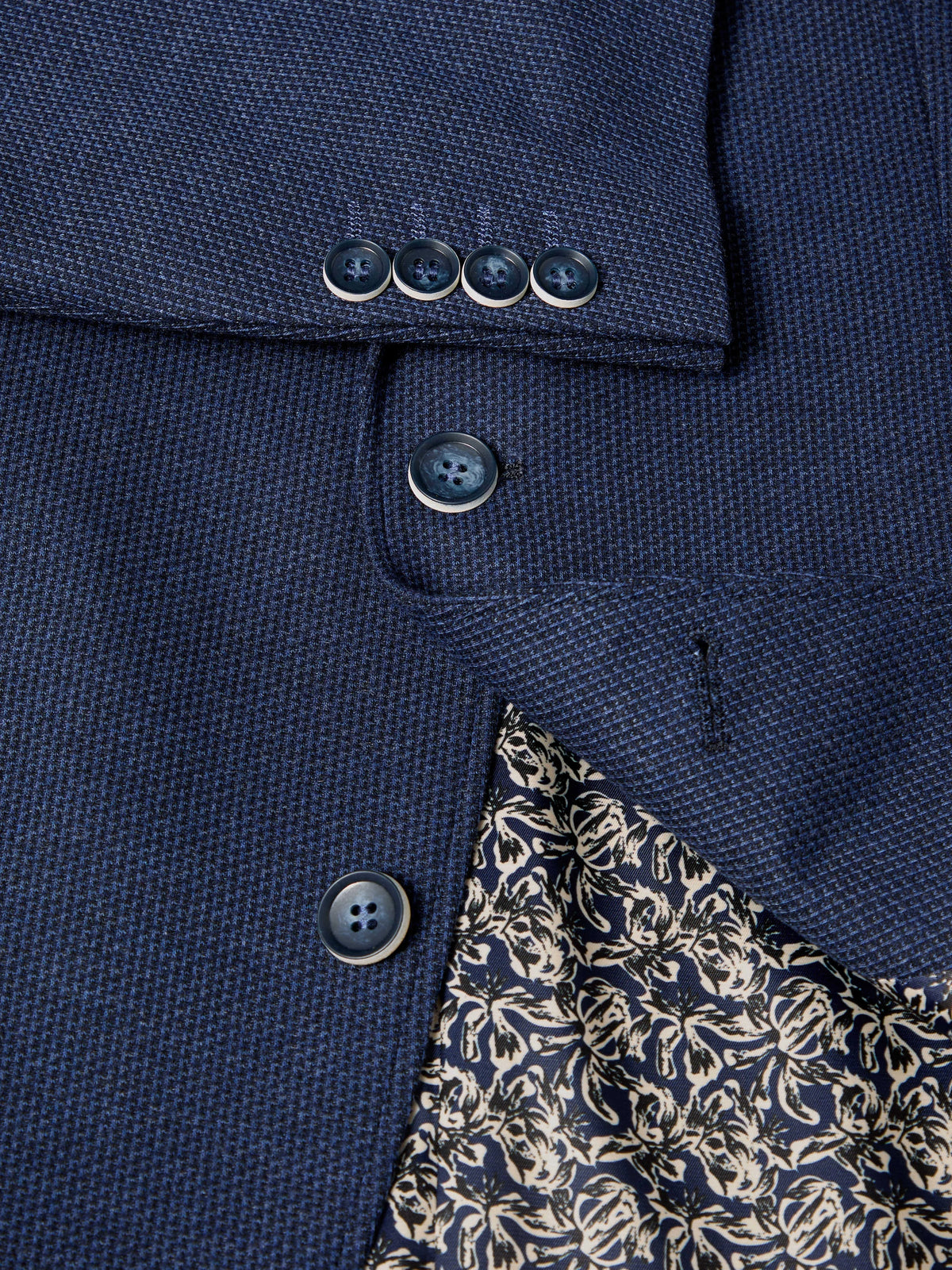 Close-up of a navy blue textured blazer fabric with dark buttons and a partially visible cream floral lining.