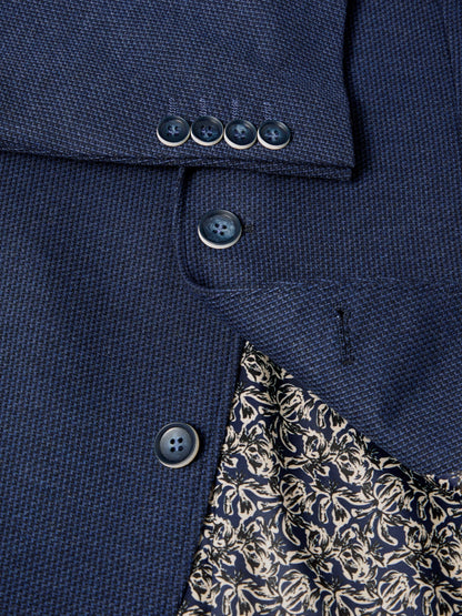 Close-up of a navy blue textured blazer fabric with dark buttons and a partially visible cream floral lining.