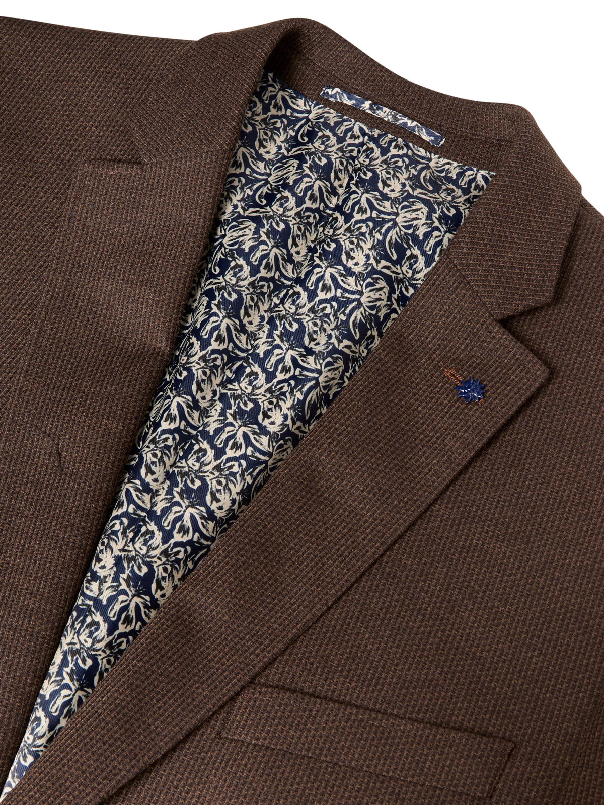 Close-up of a brown textured blazer jacket with a patterned navy and beige lining visible inside the collar, and a small embroidered logo on the lapel.