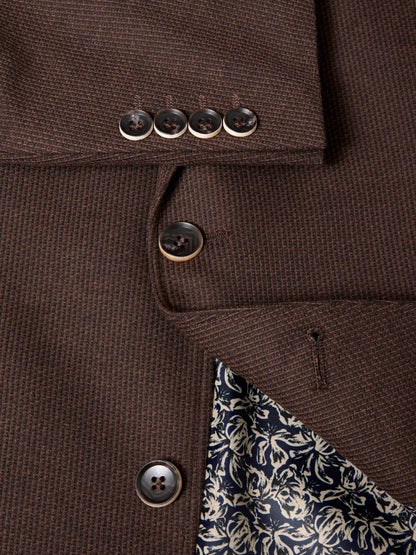 Close-up of a brown textured wool-blend blazer showing the buttoned cuff with four buttons, the front button closure, and a patterned navy and cream lining.