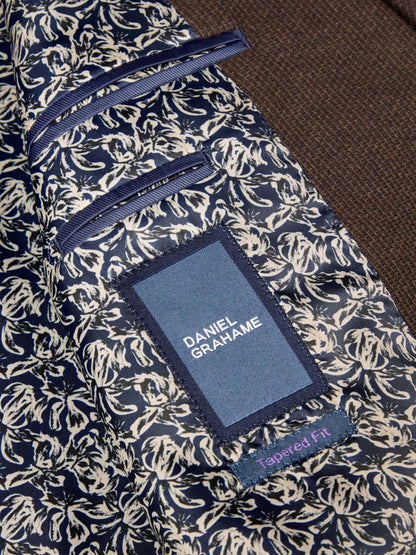Close-up of a Daniel Grahame tailored fit suit interior, showing a navy and beige floral patterned lining with a blue brand patch and a brown jacket fabric.
