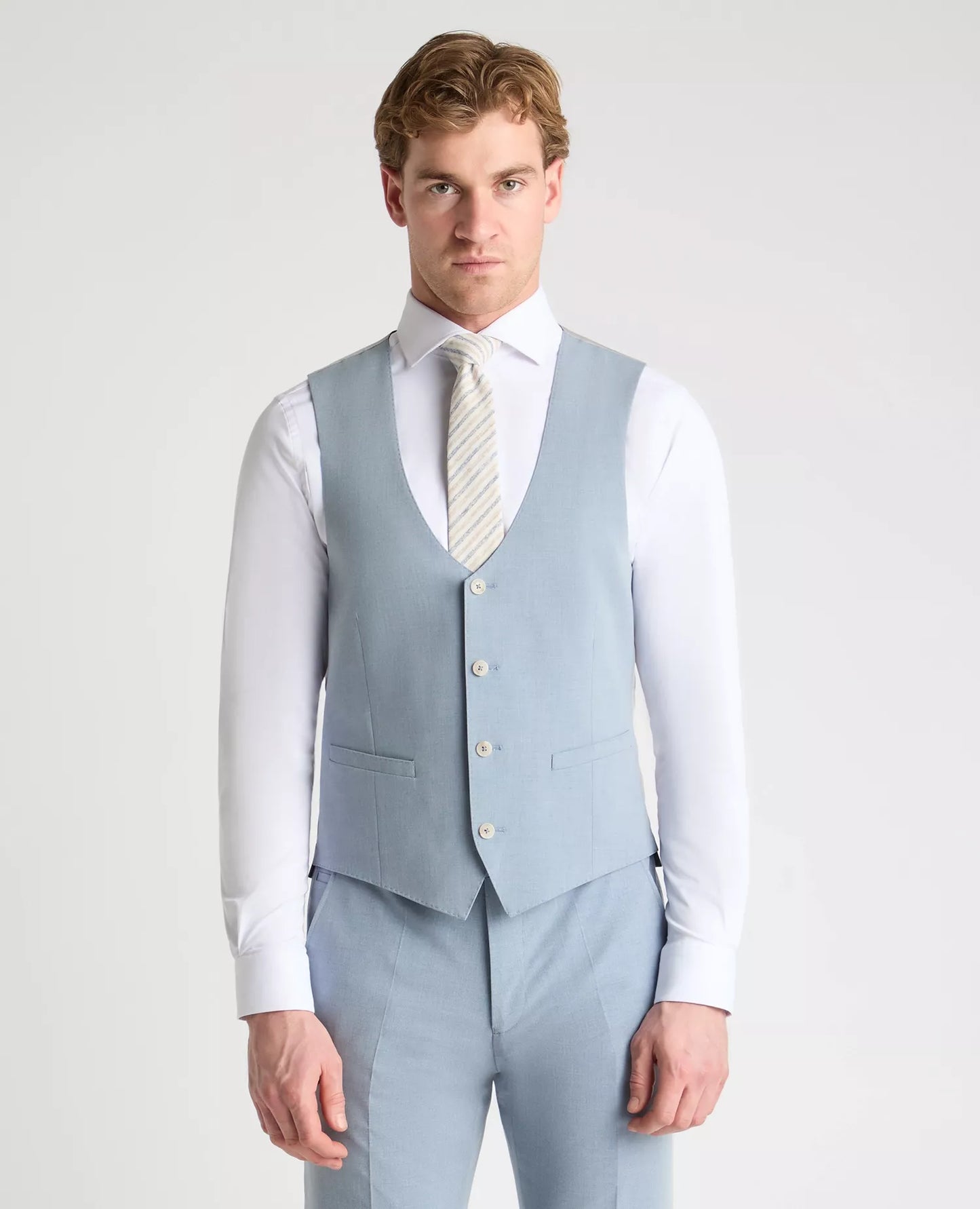 Man wearing a light blue suit vest and pants with a white shirt and tie on a plain background
