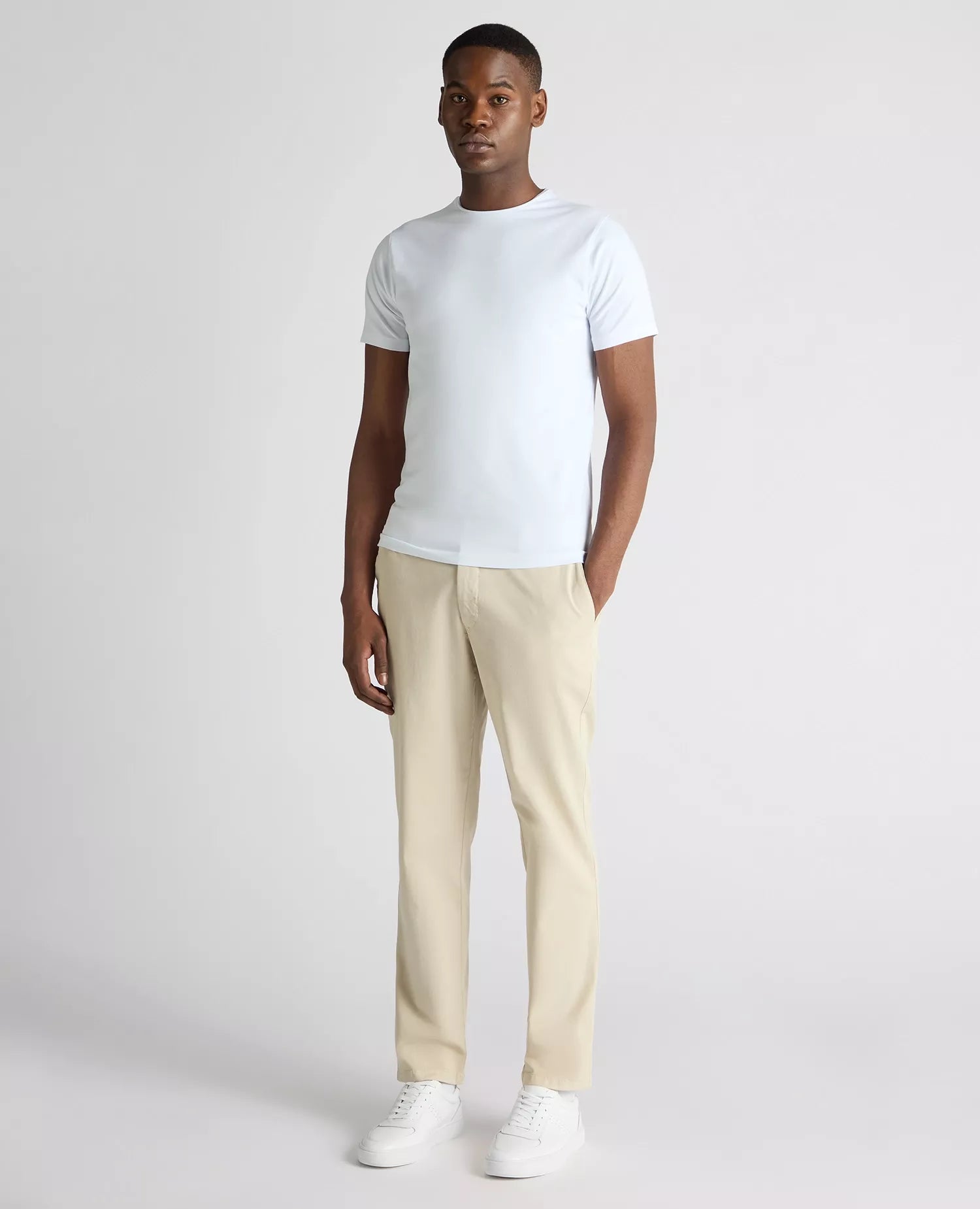 Man wearing a white t-shirt and beige pants on a light gray background