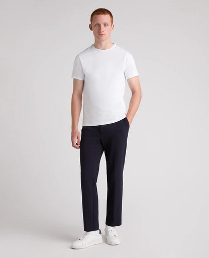 A man modeling a white short-sleeve crewneck t-shirt, dark navy trousers, and white sneakers against a light gray studio background.