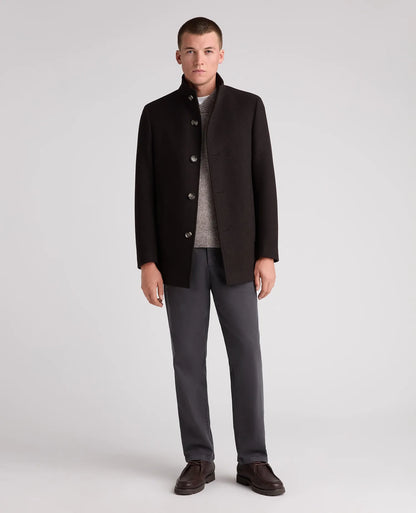 A man modeling a dark brown wool-blend coat with a stand collar, worn over a gray knit sweater, dark gray trousers, and brown leather loafers, shot against a light gray studio background.