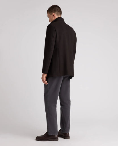 A man shown from the back wearing a dark brown blazer, dark gray trousers, and dark brown leather shoes, standing against a light gray studio background.