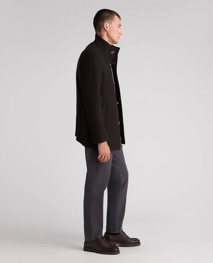 A man in profile wearing a black wool-blend coat, dark gray trousers, and dark brown leather shoes, standing against a light gray studio background.