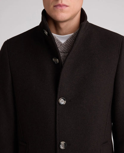 Close-up of a man wearing a dark brown wool-blend coat with a high stand collar, three front buttons, and a gray knit sweater underneath, against a light gray studio background.