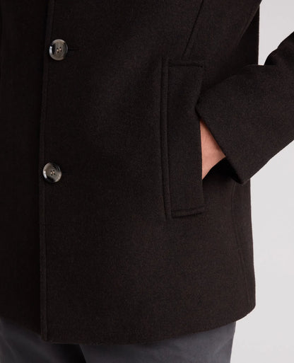 Close-up of a dark brown wool-blend coat with a double-breasted button closure and a side pocket, worn by a model whose hand is in the pocket.