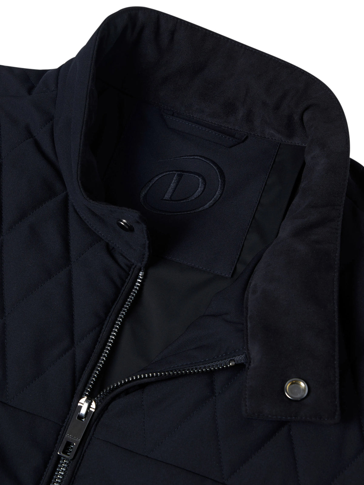 Close-up of a black quilted jacket with a stand-up collar, showing a tonal embossed logo patch on the inside neck, a front zipper, and a snap-button flap.