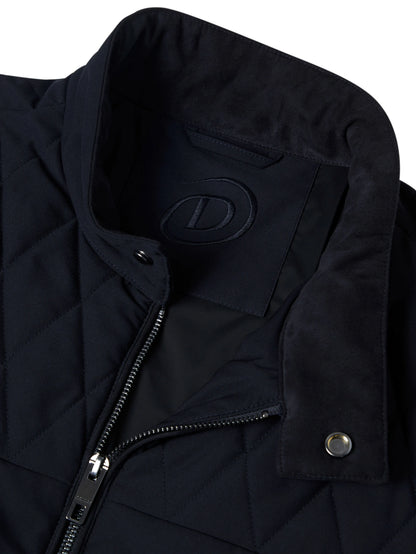 Close-up of a black quilted jacket with a stand-up collar, showing a tonal embossed logo patch on the inside neck, a front zipper, and a snap-button flap.