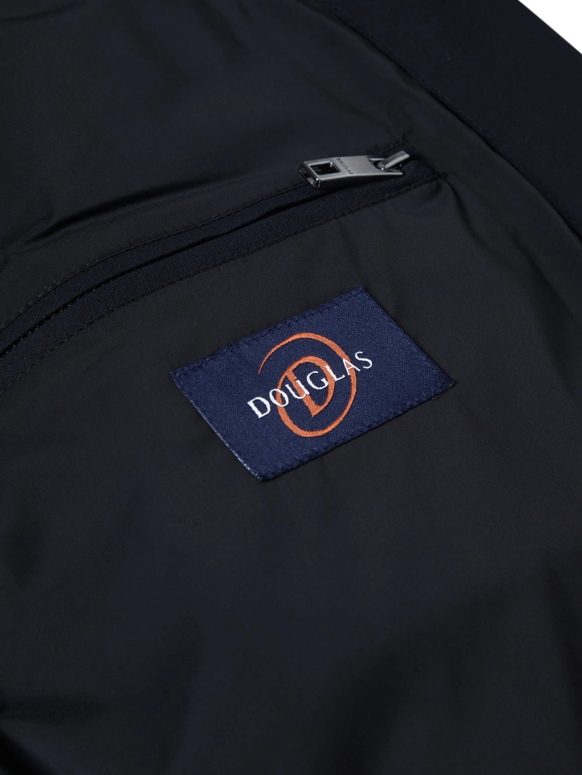 Close-up of a dark navy jacket or bag pocket with a silver zipper and a blue embroidered Douglas logo patch.