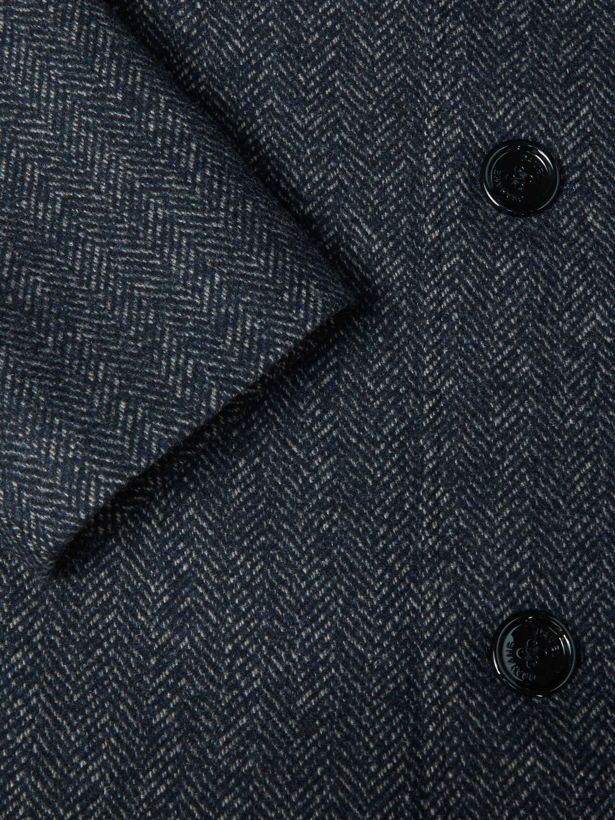 Close-up of a dark navy blue herringbone tweed fabric with black buttons.