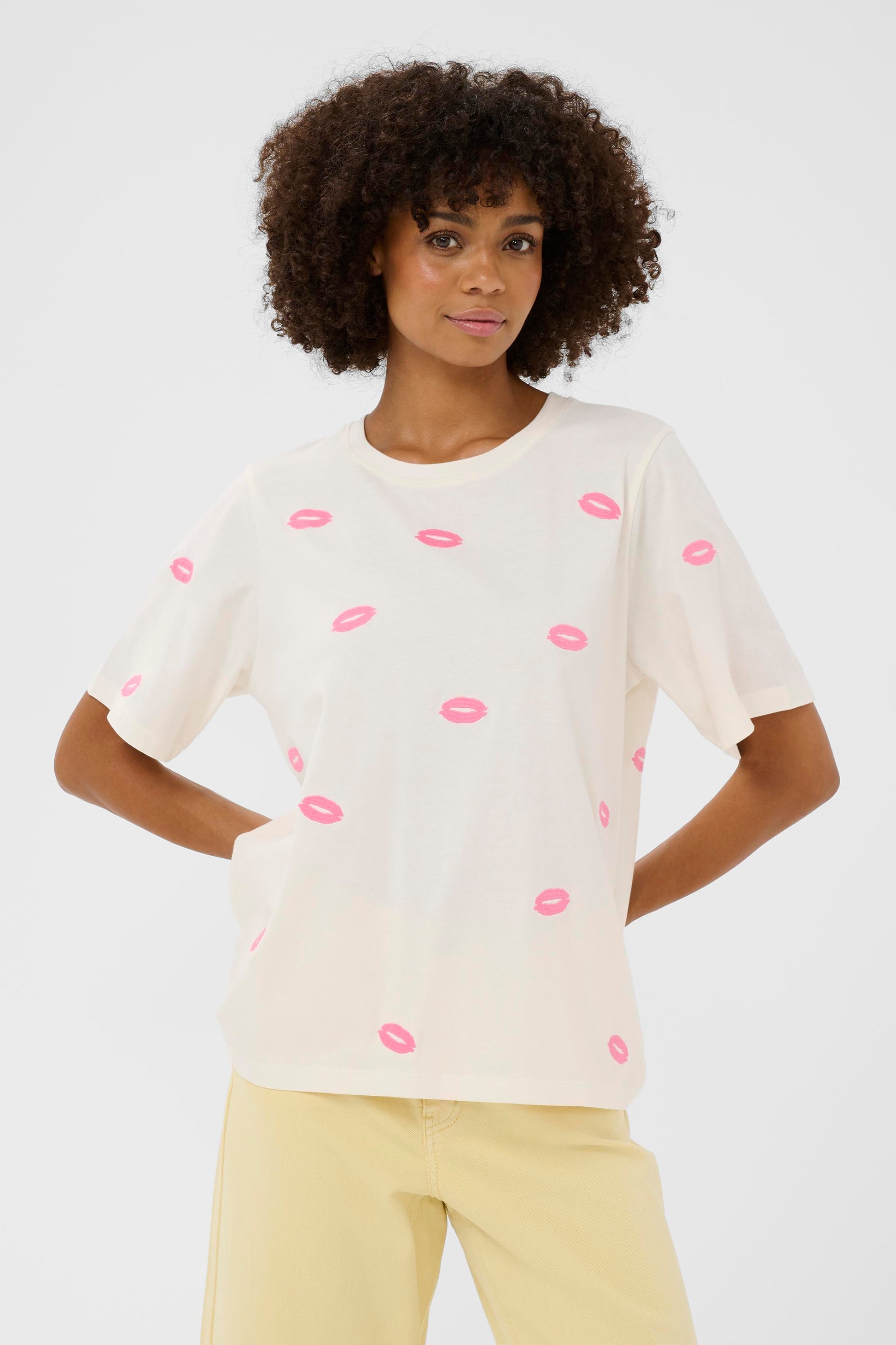 Woman wearing a white t-shirt with pink lip prints on a plain background
