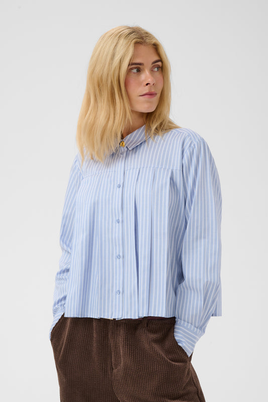 Woman wearing a light blue striped shirt and brown pants on a white background