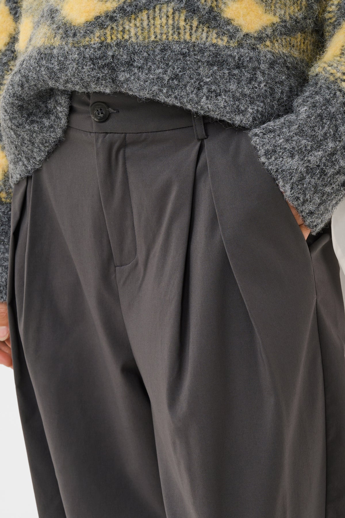 Close-up of a person wearing dark charcoal gray pleated trousers and a fuzzy gray sweater with yellow patterned knit details.