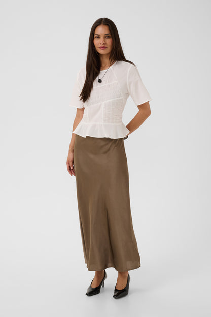 A woman modeling a white short-sleeve blouse with a textured front and a peplum hem, paired with a brown maxi skirt and black heels, against a light gray studio background.
