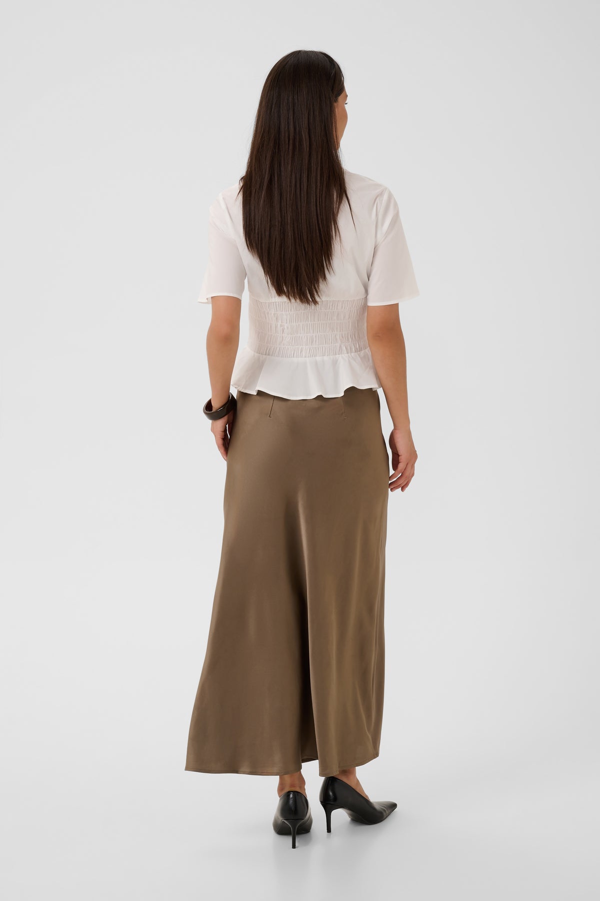 A woman shown from the back wearing a white smocked short-sleeve blouse and a brown wide-leg midi skirt, paired with black heels, against a light gray studio background.