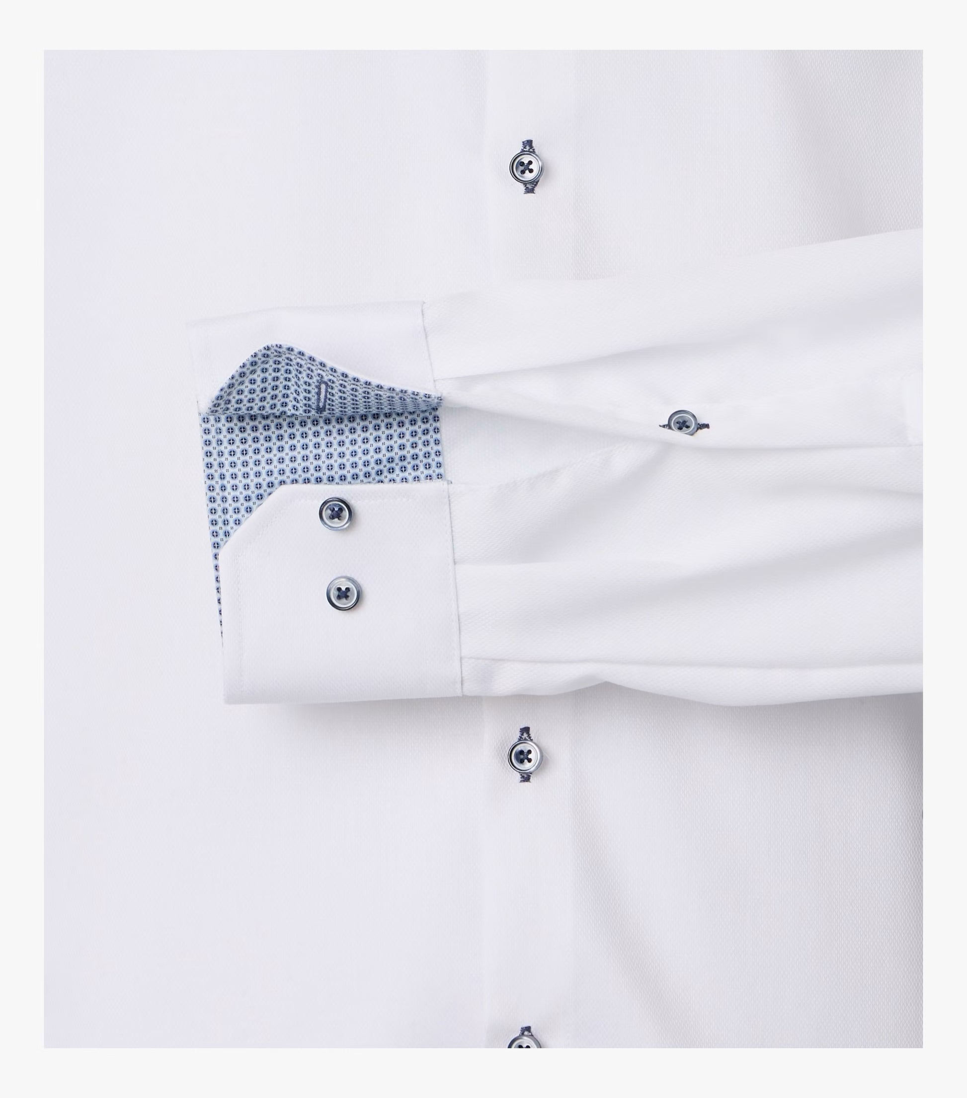Close-up of a white dress shirt cuff with silver buttons and a blue patterned inner lining, shown against a white background.