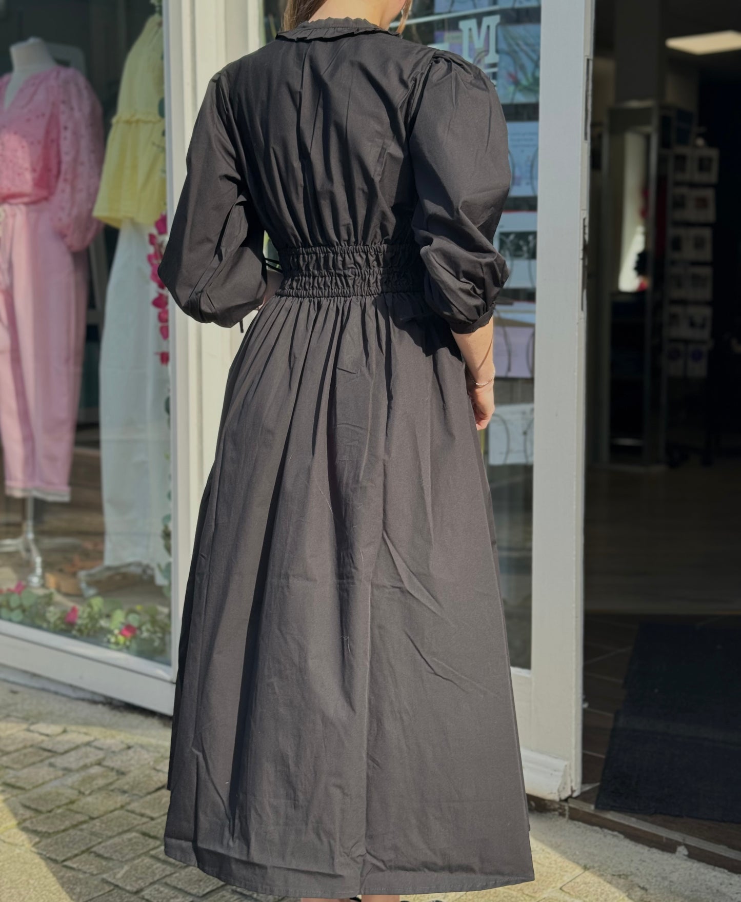 Person wearing a long black dress standing outside a store with clothing displayed in the window.
