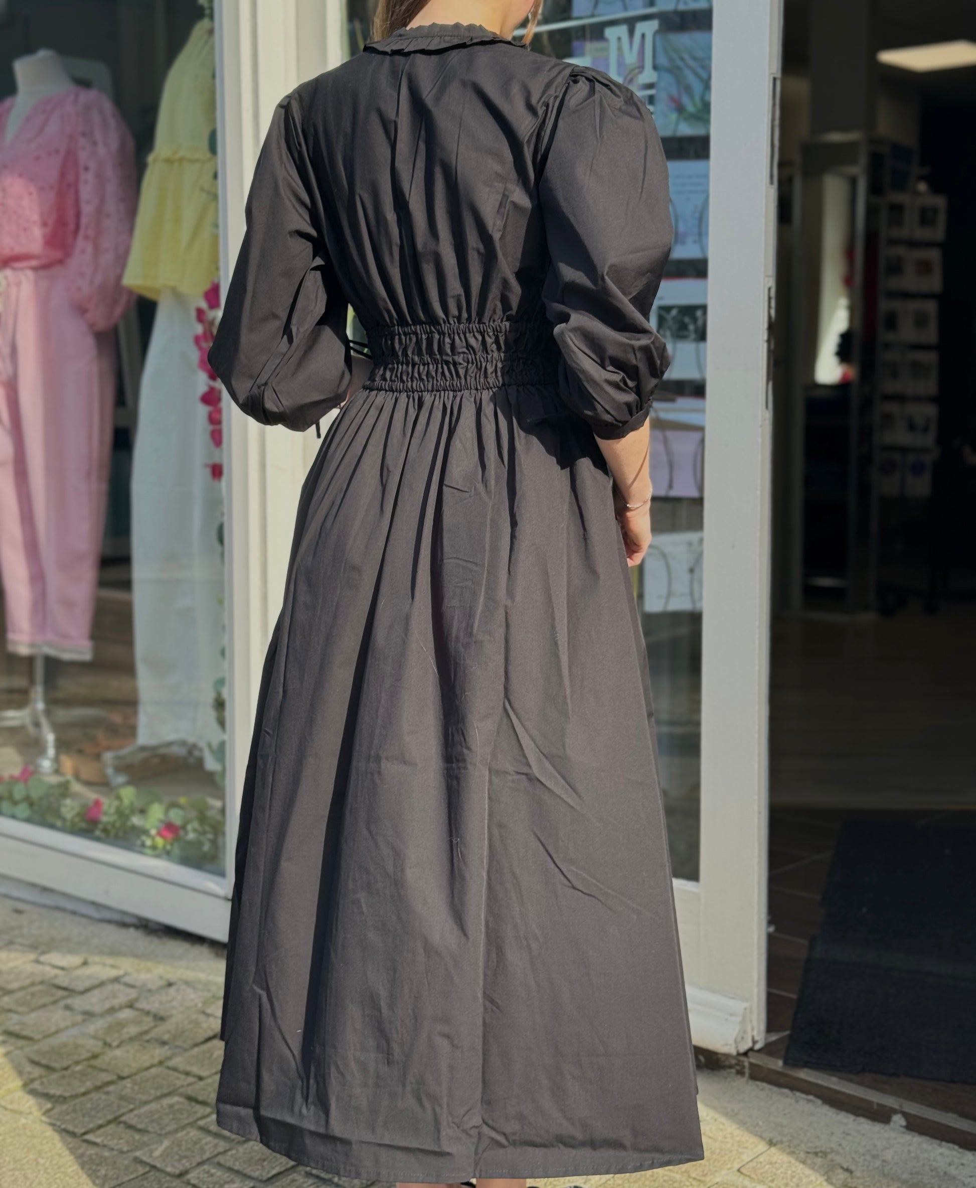 Person wearing a long black dress standing outside a store with clothing displayed in the window.