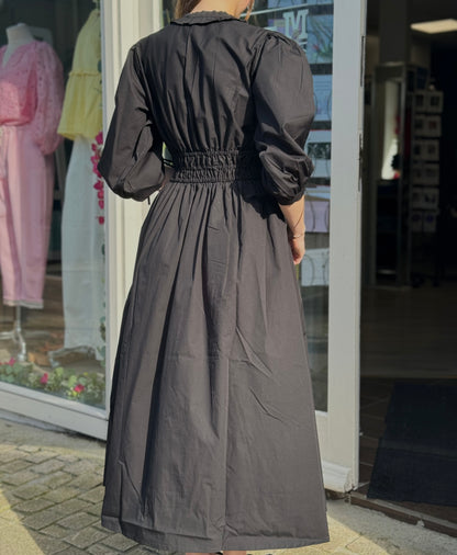 Person wearing a long black dress standing outside a store with clothing displayed in the window.