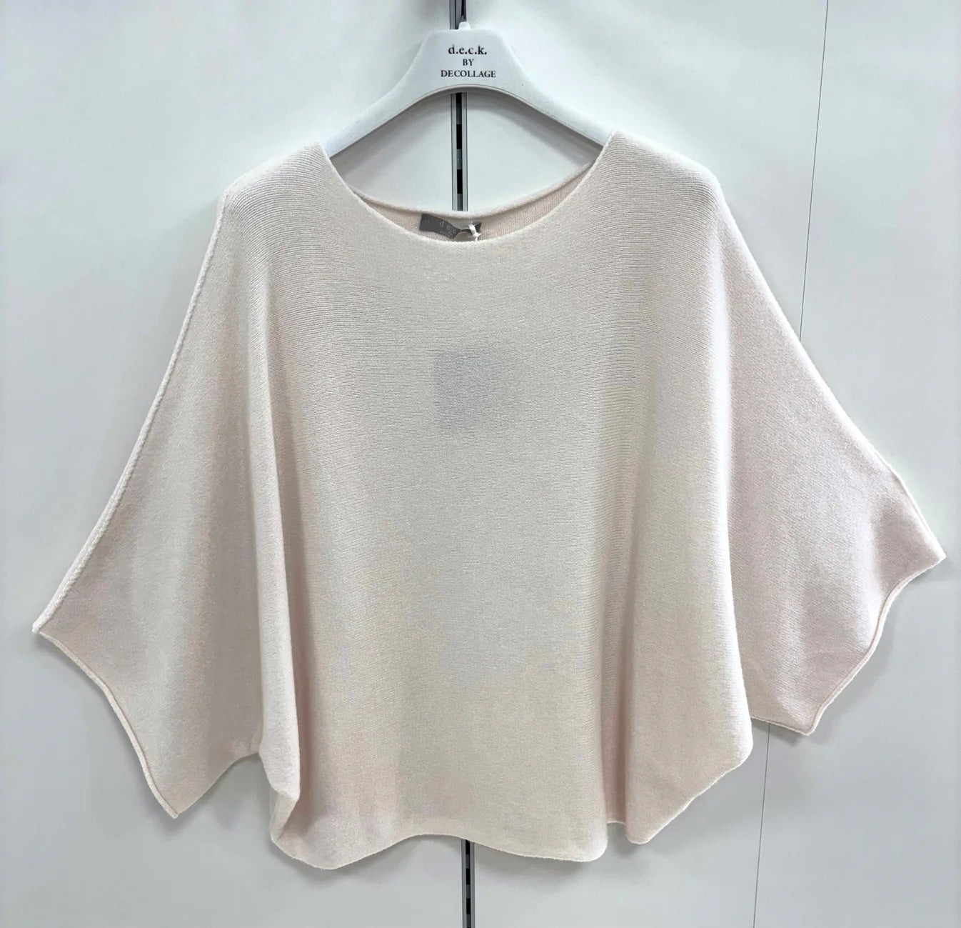Beige poncho-style top on a hanger against a white background