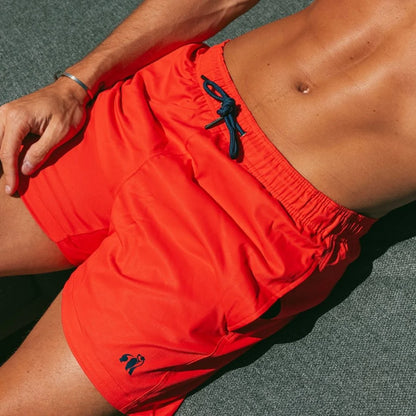 Person wearing bright orange swim shorts with a brand logo on a dark surface