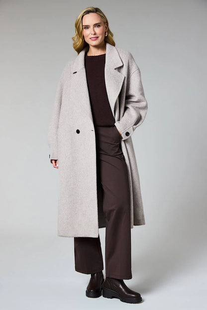 A woman modeling a long, double-breasted light gray wool-blend coat over a dark brown top and matching wide-leg trousers, paired with dark brown ankle boots, against a neutral light gray studio background.