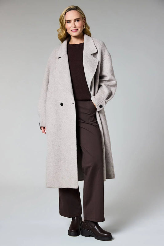 A woman modeling a long, double-breasted light gray wool-blend coat over a dark brown top and matching wide-leg trousers, paired with dark brown ankle boots, against a neutral light gray studio background.