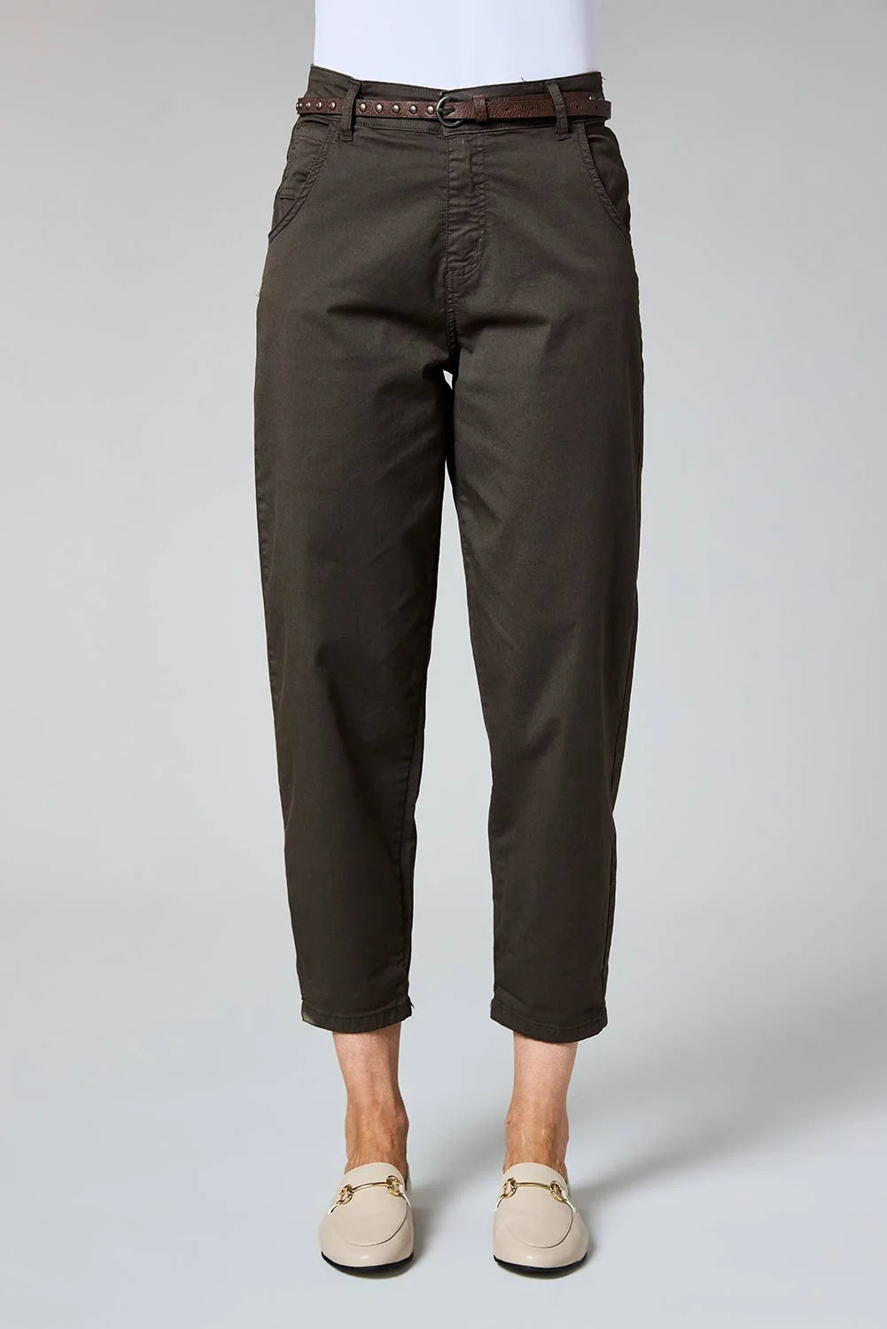 A person wearing dark brown cropped trousers with a matching brown belt, paired with beige loafers, shown from the waist down on a light gray studio background.