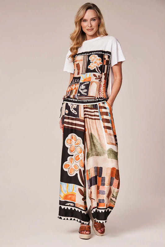 Woman wearing a white t-shirt with a colorful graphic design and patterned pants on a beige background