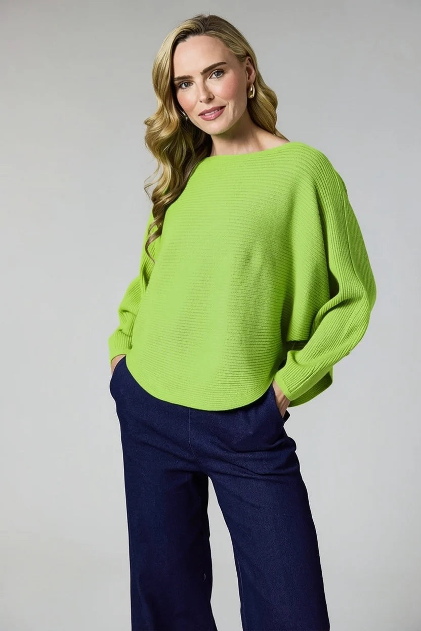 A woman modeling a bright lime green ribbed knit sweater with a boat neckline and balloon sleeves, paired with dark navy wide-leg trousers, against a light gray studio background.