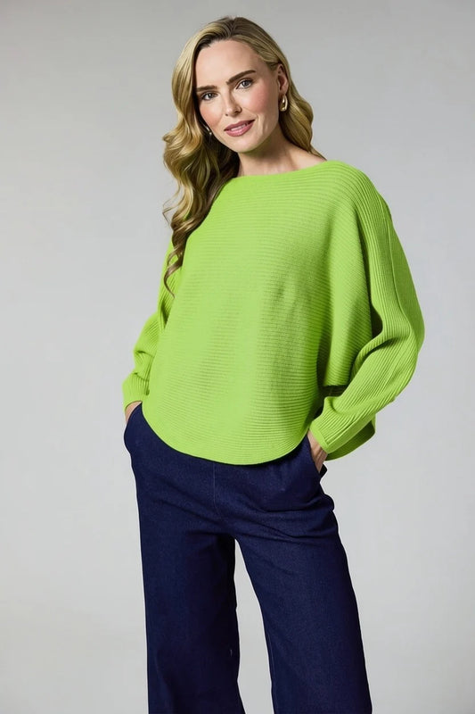 A woman modeling a bright lime green ribbed knit sweater with a boat neckline and balloon sleeves, paired with dark navy wide-leg trousers, against a light gray studio background.