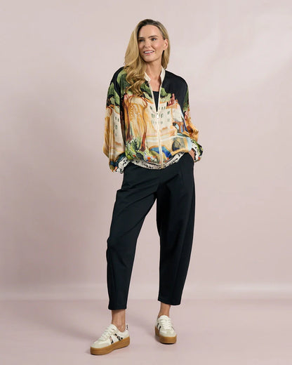 Woman wearing a colorful patterned shirt and black pants on a plain background